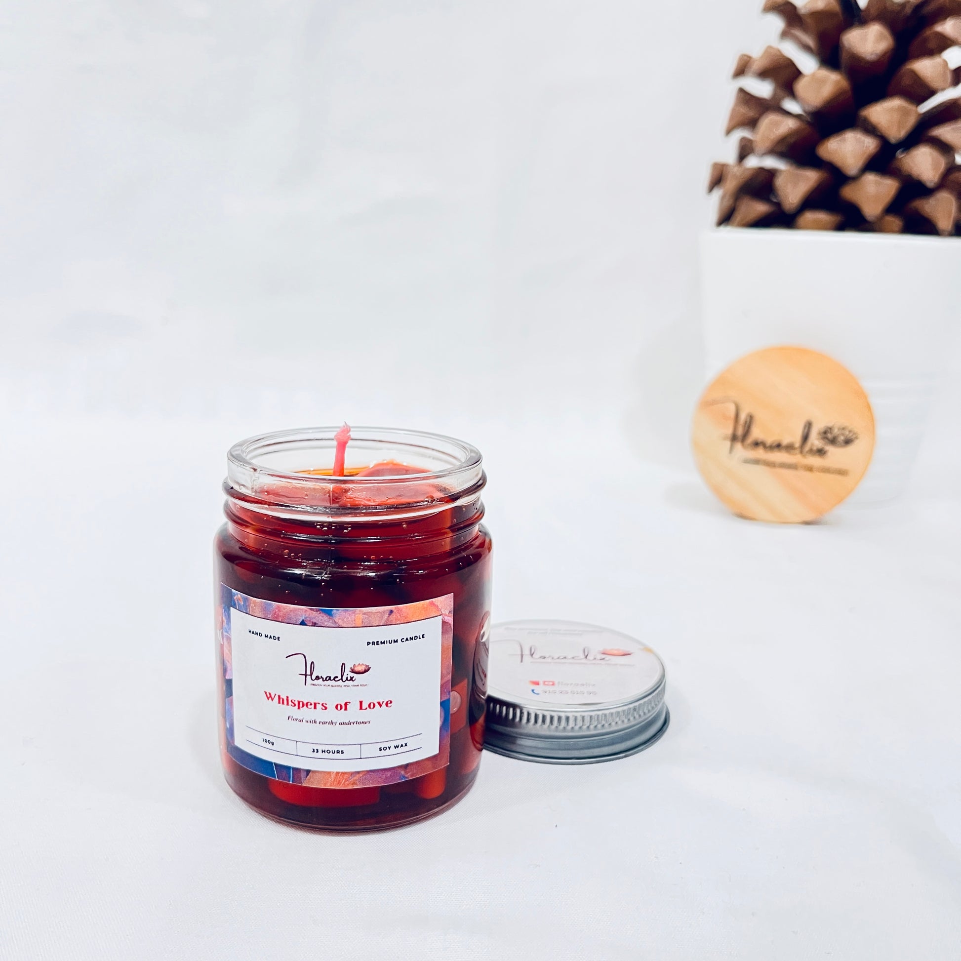 Jaivik Store Whispers of Love soy wax jar candle, 100g, with lid open, displayed against a pine fruit backdrop for natural charm